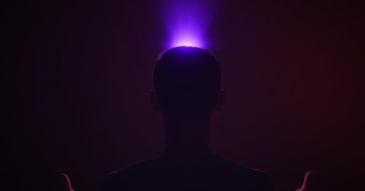 A person meditating seen from behind with soft violet light rising from the crown of the head